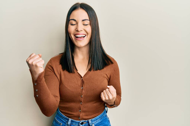 Young brunette woman wearing casual clothes celebrating surprised and amazed for success with arms raised and eyes closed  - Photo, Image