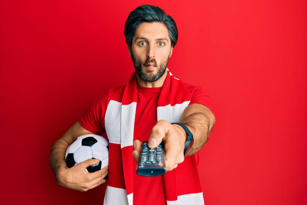 Genç İspanyol futbolcu holigan elinde top TV kontrolü kullanarak balık suratlı ve şaşı bakışlı çılgın ve komik gözler yapıyor..  - Fotoğraf, Görsel