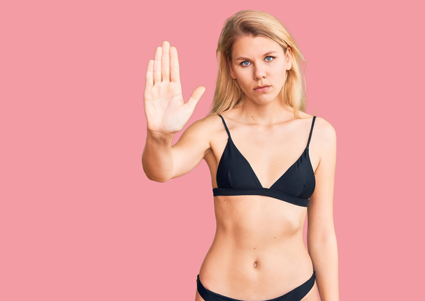 Jonge mooie blonde vrouw in bikini doet stoppen met zingen met palm van de hand. waarschuwingsuitdrukking met negatief en ernstig gebaar op het gezicht.  - Foto, afbeelding