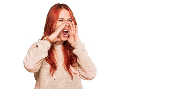 Jeune femme rousse portant un pull d'hiver décontracté criant en colère à haute voix avec les mains sur la bouche  - Photo, image
