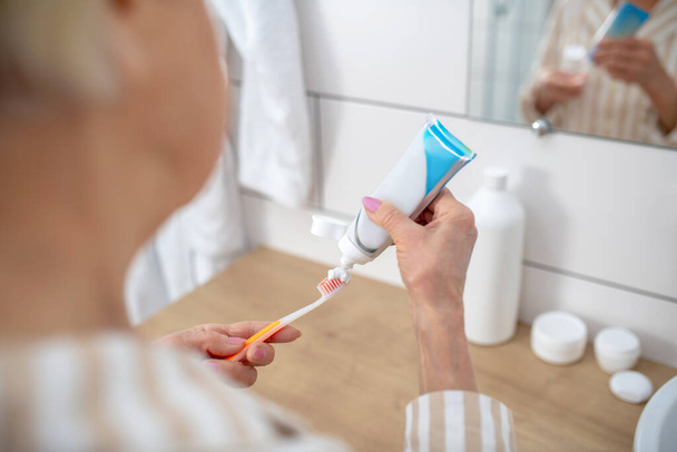 Imagen de cerca de una mujer apretando pasta de dientes y un cepillo de dientes - Foto, imagen