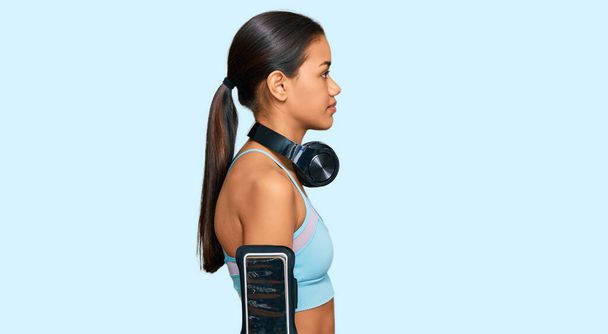 Beautiful hispanic woman wearing sportswear and headphones looking to side, relax profile pose with natural face with confident smile.  - Foto, afbeelding