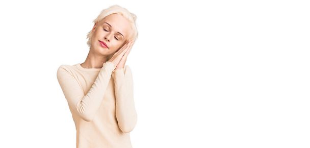 Young blonde woman wearing casual clothes sleeping tired dreaming and posing with hands together while smiling with closed eyes.  - Foto, Imagem