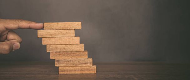 Detailní záběr prstem tlačit dřevo blok věž naskládané na schodišti krok s opatrností, aby se zabránilo zhroucení nebo zhroucení koncepce řízení finančních rizik a strategického plánování. - Fotografie, Obrázek