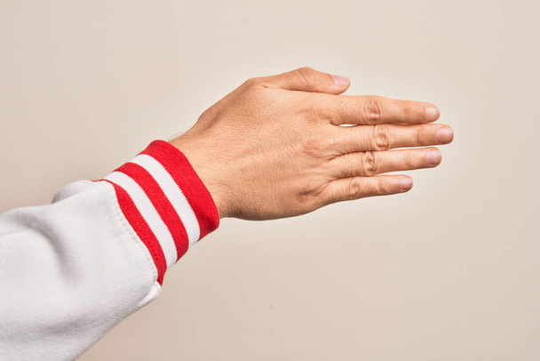 Χέρι καυκάσιου νεαρού άνδρα που δείχνει τα δάχτυλά του πάνω από απομονωμένο λευκό φόντο που εκτείνεται και φτάνει με ανοιχτό χέρι για χειραψία, δείχνοντας το πίσω μέρος του χεριού - Φωτογραφία, εικόνα