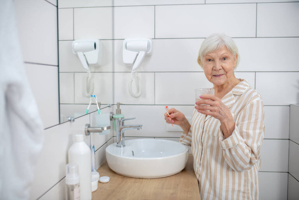 Aged woman doing morning procedures in the bathroom - Фото, изображение