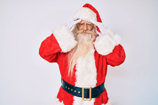 Старик с седыми волосами и длинной бородой в костюме Санта Клауса с подтяжками с рукой на голове от боли в голове из-за стресса. страдает мигренью.  - Фото, изображение