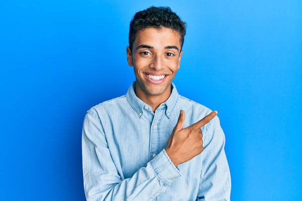 Joven hombre afroamericano guapo usando ropa casual sonriendo alegre señalando con la mano y el dedo hacia arriba a un lado  - Foto, Imagen
