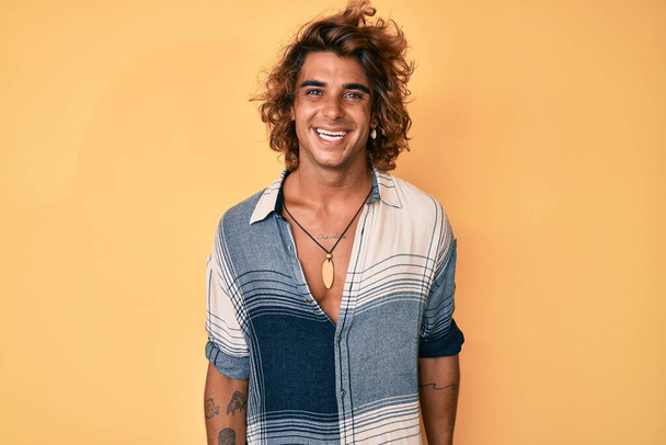 Νεαρός ισπανόφωνος άντρας με καλοκαιρινό στυλ που δείχνει θετικός και χαρούμενος στέκεται και χαμογελάει με ένα σίγουρο χαμόγελο που δείχνει δόντια  - Φωτογραφία, εικόνα
