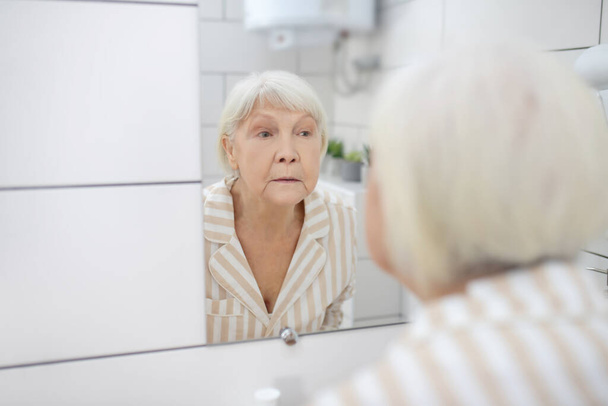 Gray-haired woman looking in the mirror in the bathroom - Foto, immagini
