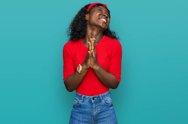 Mooie Afrikaanse jonge vrouw in casual kleding bedelend en biddend met de handen samen met hoop uitdrukking op het gezicht zeer emotioneel en bezorgd. bedelen.  - Foto, afbeelding
