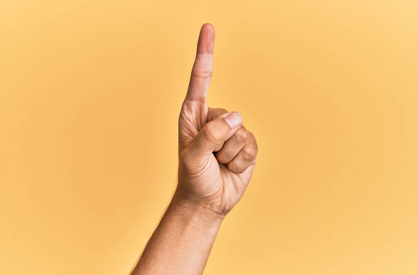 Χέρι και χέρι του καυκάσιου ανθρώπου πάνω από κίτρινο απομονωμένο φόντο καταμέτρηση νούμερο ένα χρησιμοποιώντας δείκτη, που δείχνει την ιδέα και την κατανόηση  - Φωτογραφία, εικόνα