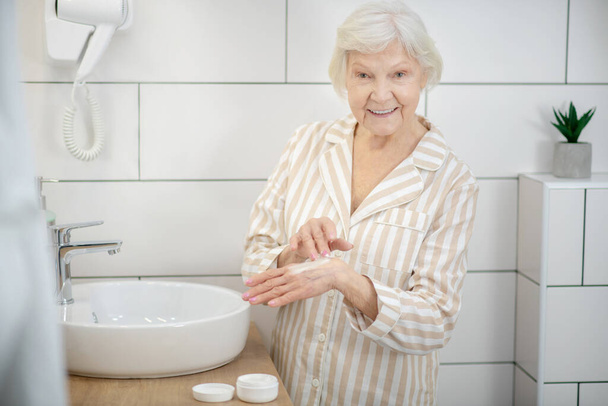 Elderly smiling woman applying hand cream on hands - Foto, Imagen