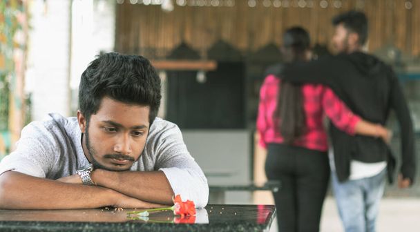 Smutny młody człowiek widząc czerwoną różę podczas walentynek z powodu złamanego lub zdradzonego związku ze swoją dziewczyną - Zdjęcie, obraz