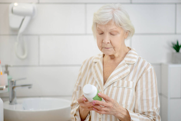Lyhyttukkainen vanha nainen, jolla on pullo, jossa on vitamiineja käsissään - Valokuva, kuva