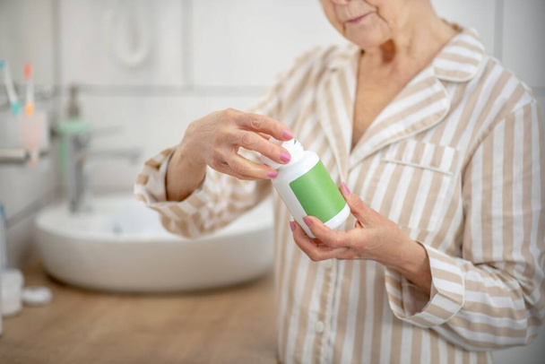 Mujer en pijama sosteniendo un frasco con pastillas en las manos - Foto, Imagen