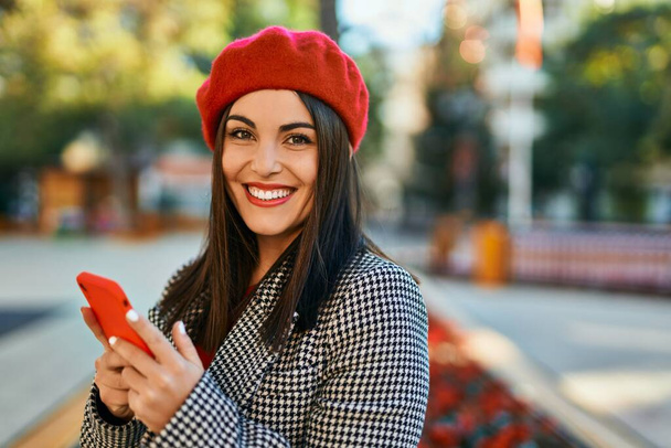 Junge hispanische Frau lächelt glücklich mit Smartphone in die Stadt. - Foto, Bild
