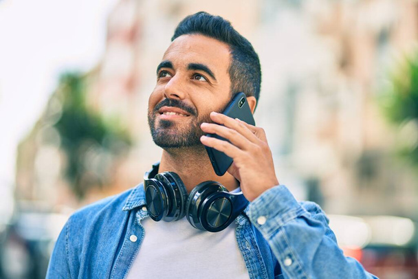 Mladý hispánec se šťastně usmívá a mluví po telefonu ve městě. - Fotografie, Obrázek