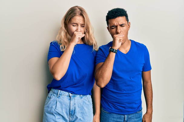 Jeune couple interracial portant des vêtements décontractés se sentant mal et toussant comme symptôme de rhume ou de bronchite. concept de soins de santé.  - Photo, image
