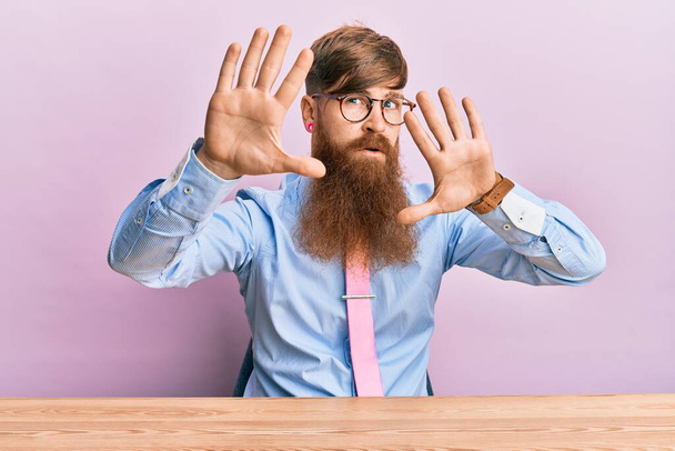 Young irish redhead man wearing business shirt and tie sitting on the table doing frame using hands palms and fingers, camera perspective  - Fotografie, Obrázek