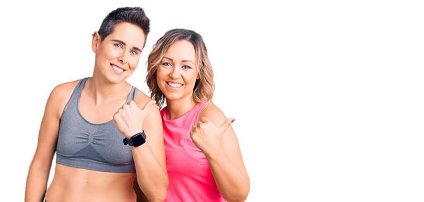 Coppia di donne che indossano abbigliamento sportivo indicando la schiena dietro con mano e pollice in su, sorridendo fiducioso  - Foto, immagini