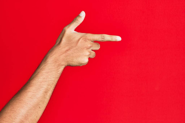 Braço de branco branco jovem sobre vermelho isolado fundo apontando com o dedo indicador para o lado, sugerindo e selecionando uma escolha  - Foto, Imagem