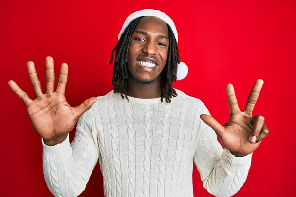 Africano americano com tranças vestindo chapéu de Natal mostrando e apontando para cima com os dedos número oito, sorrindo confiante e feliz.  - Foto, Imagem