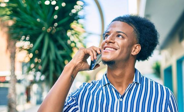 Genç Afrikalı Amerikalı gülümseyen mutlu bir adam şehirdeki akıllı telefondan konuşuyor.. - Fotoğraf, Görsel