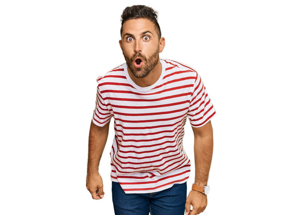 Handsome man with beard wearing striped tshirt scared and amazed with open mouth for surprise, disbelief face  - Foto, imagen