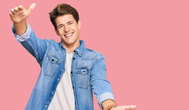 Handsome caucasian man wearing casual denim jacket looking at the camera smiling with open arms for hug. cheerful expression embracing happiness.  - Photo, Image