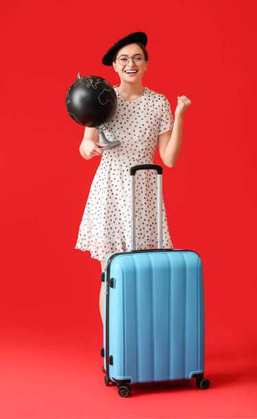 Happy female tourist with globe and luggage on color background - Photo, Image