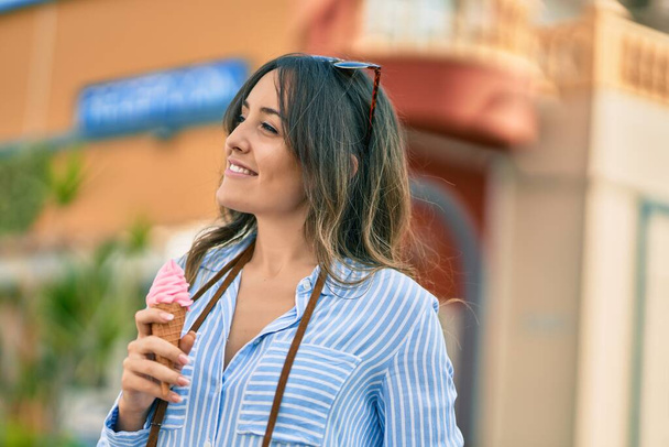 Молодая латиноамериканка, улыбающаяся, счастливо поедая мороженое в городе. - Фото, изображение