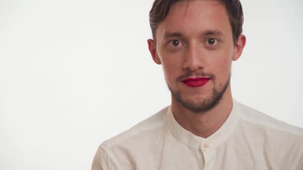 Uncertain person with dark brown beard, hair wear shirt, red lipstick on lips, smiles like a fool isolated on white wall background. Portrait of metrosexual or gay business man with makeup close up. - Felvétel, videó