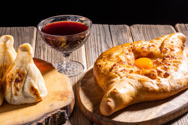 Adjarian khinkali and khachapuri with wine and sauce on a wooden table and stands, close-up. - Фото, изображение