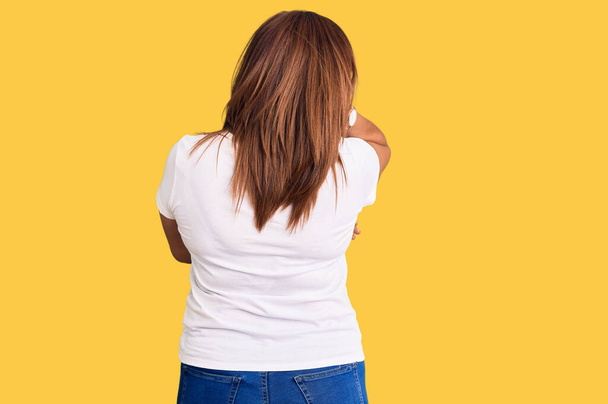 Středního věku latinsky žena na sobě ležérní bílé tričko pozpátku přemýšlet o pochybách s rukou na hlavě  - Fotografie, Obrázek