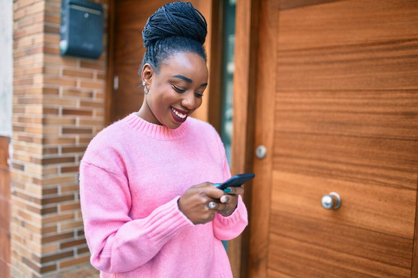 Nuori afrikkalainen amerikkalainen nainen hymyilee onnellisena älypuhelimella kaupungissa. - Valokuva, kuva