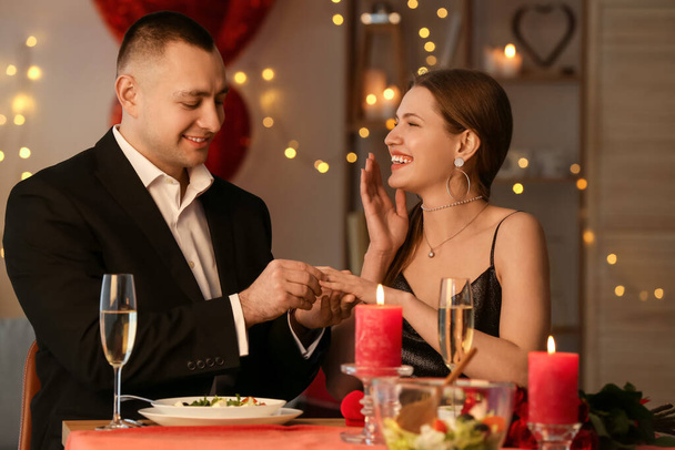 Молодий чоловік одягає обручку на палець своєї нареченої після шлюбної пропозиції в день святого Валентина вдома. - Фото, зображення