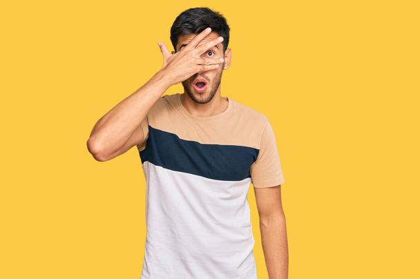 Young handsome man wearing casual clothes peeking in shock covering face and eyes with hand, looking through fingers with embarrassed expression.  - Photo, Image