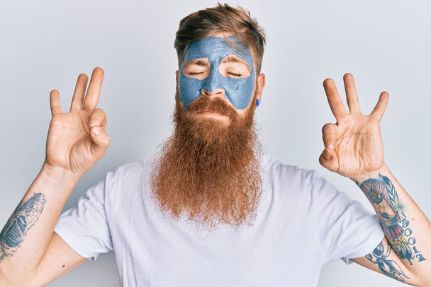 Young irish redhead man wearing facial mask relax and smiling with eyes closed doing meditation gesture with fingers. yoga concept.  - Foto, Bild