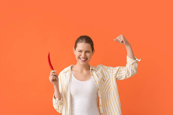 Beautiful young woman with hot chili pepper on color background - Photo, Image