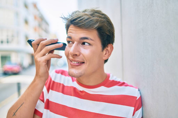 Молодий кавказький чоловік посміхається щасливим прослуховуванням аудіоповідомлень за допомогою смартфона в місті
. - Фото, зображення