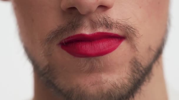 Vista de cerca de la linda boca masculina caucásica con barba y bigote. Hombre llevar lápiz labial rojo en los labios, golpe beso sobre fondo blanco. Concepto de protección de los derechos de la comunidad LGBT, manifestación clara - Metraje, vídeo