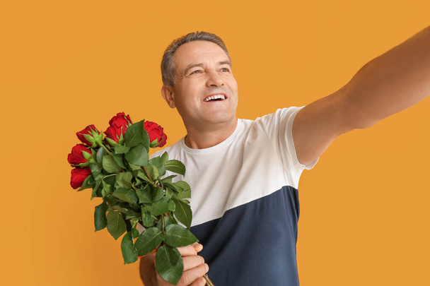 Mature man with bouquet of beautiful flowers taking selfie on color background - Fotó, kép