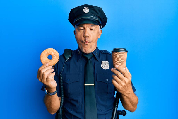 Handsome middle age mature police man eating donut and drinking coffee making fish face with mouth and squinting eyes, crazy and comical.  - Photo, Image