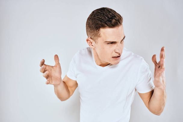 Emocional hombre gestos con sus manos desagrado blanco camiseta fondo claro - Foto, Imagen