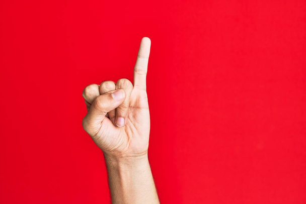 Рука белого белого кавказца на красном изолированном фоне показывает мизинец в качестве обещания на мизинце, номер один  - Фото, изображение