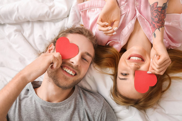 赤の心を持つ若いカップルベッドの上のビューに横たわっている。バレンタインデーのお祝い - 写真・画像