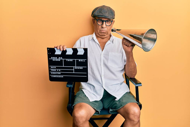 Handsome mature director man holding video film clapboard and louder skeptic and nervous, frowning upset because of problem. negative person.  - Photo, Image