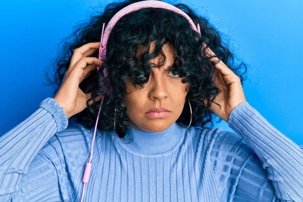 Young hispanic woman listening to music using headphones skeptic and nervous, frowning upset because of problem. negative person.  - Photo, Image
