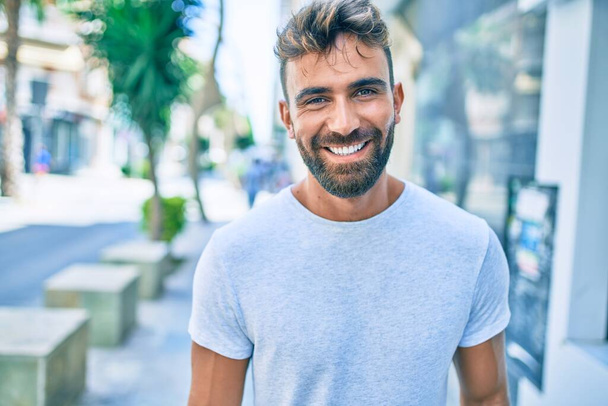 Nuori latino mies hymyilee onnellinen kävely kaupungin - Valokuva, kuva